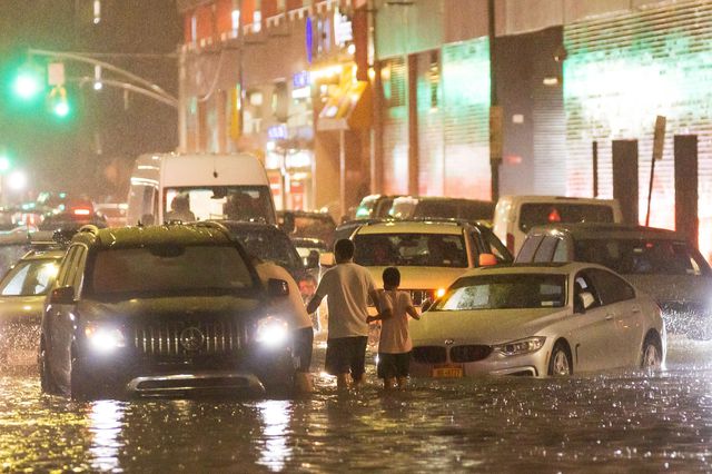 Vehicles stalled in flooded streets, with an adult and child standing in the middle of the road